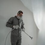 Person in protective gear painting a wall, showcasing house renovation work. - Photo by Tima Miroshnichenko on Pexels